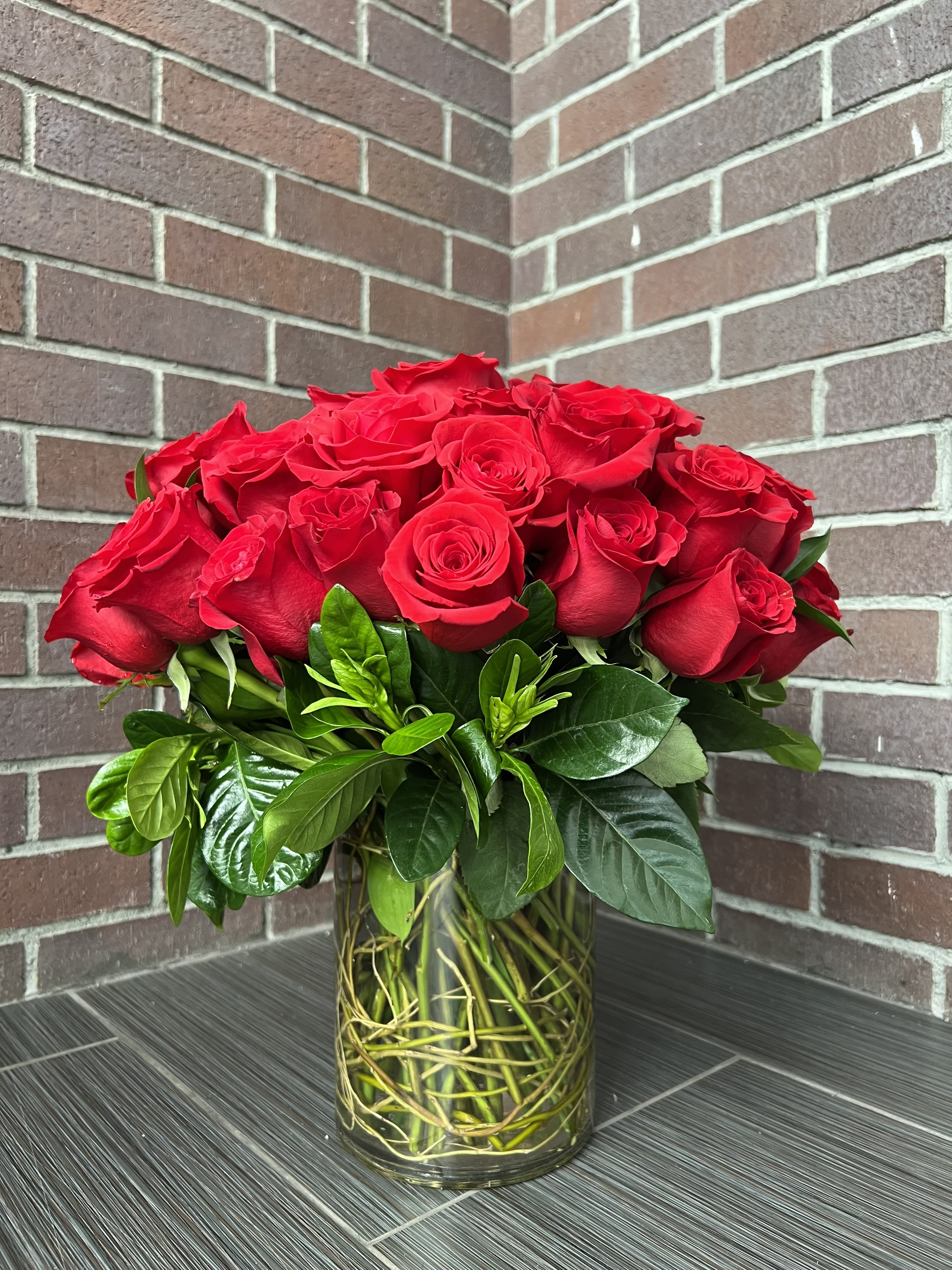 Red roses arranged in a clear glass vase with glossy greenery