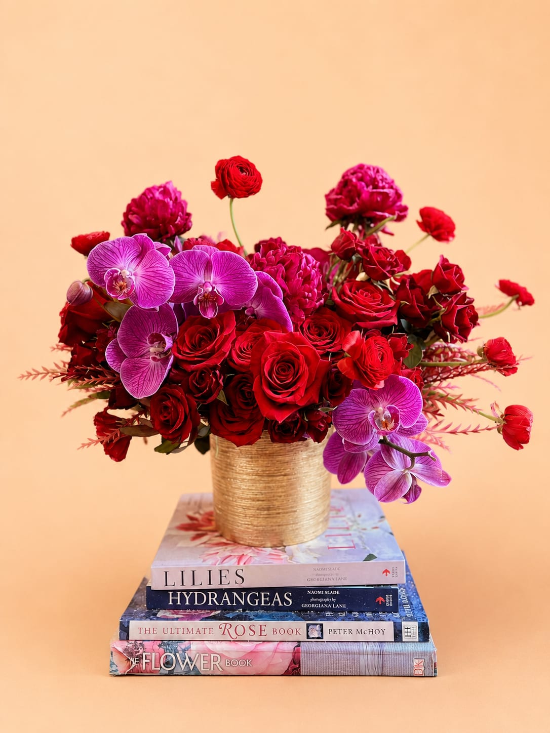 Velvet Romance - Indulge in the timeless beauty of "Velvet Romance", a luxurious floral arrangement designed to captivate. Rich crimson roses, vibrant magenta orchids, lush ranunculus, and romantic seasonal blooms come together in a radiant gold cylinder, creating a striking display of elegance &amp; passion. Overflowing with velvety textures and jewel-toned color, this arrangement is perfect for celebrating love, anniversaries, birthdays, or simply making an unforgettable statement. Sophisticated, dramatic, and undeniably romantic. "Velvet Romance" is designed to leave a lasting impression.