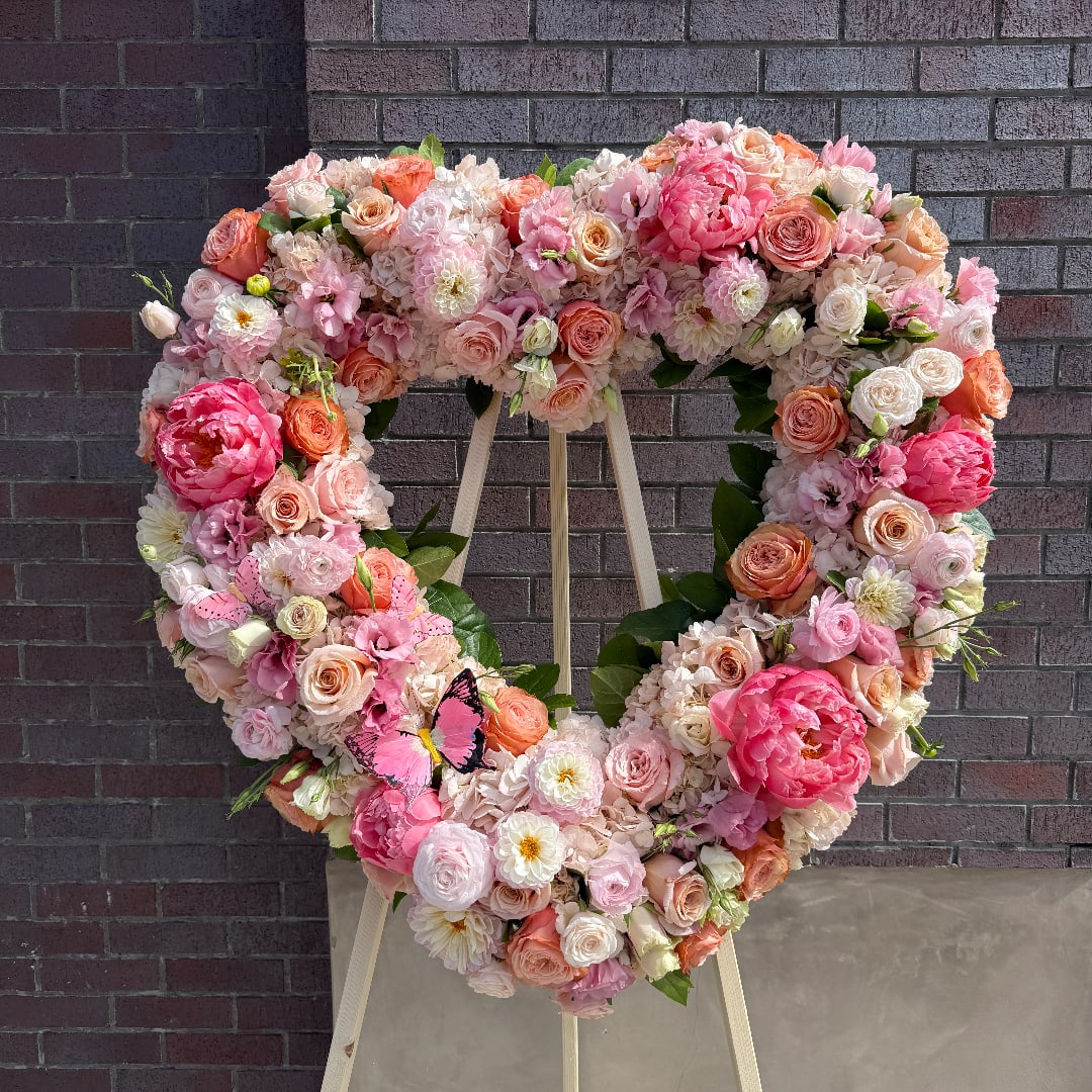 Large heart-shaped floral wreath in pink, peach, and white blooms on an easel