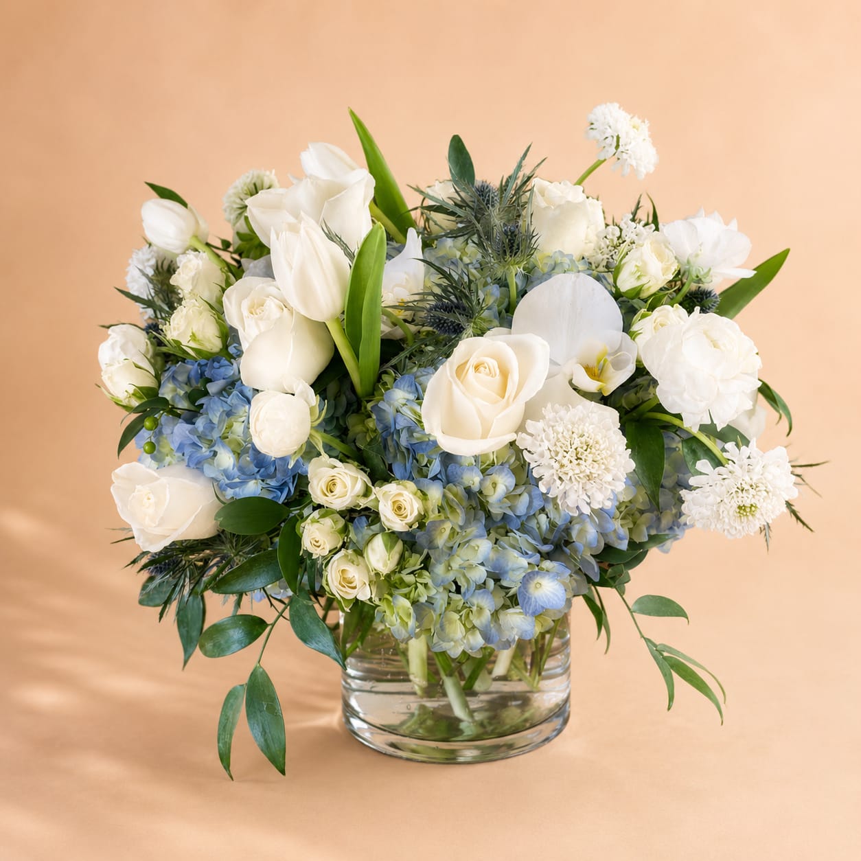 White roses and tulips with blue hydrangeas in a glass vase