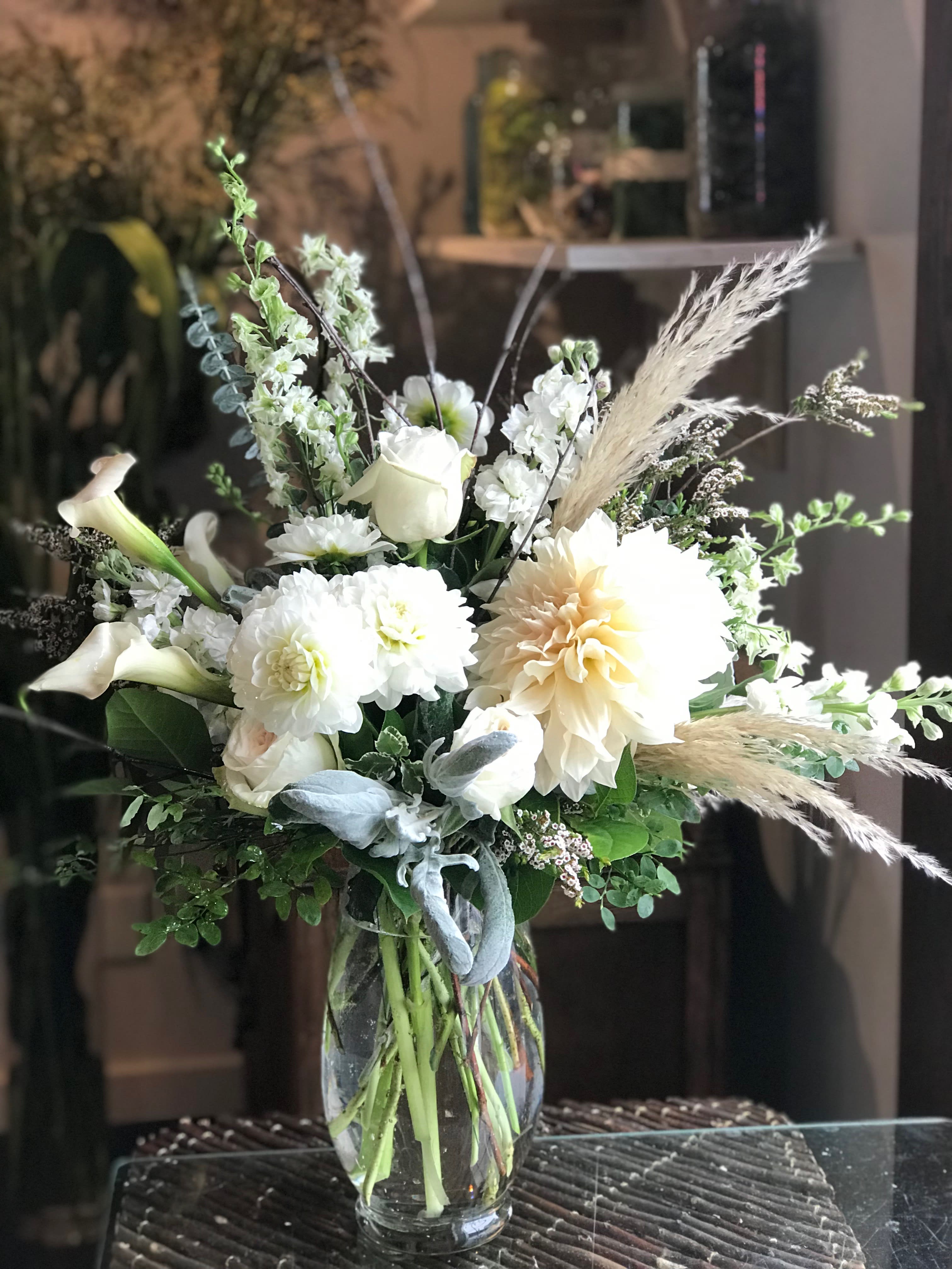 White floral arrangement in a clear glass vase with calla lilies and dahlias