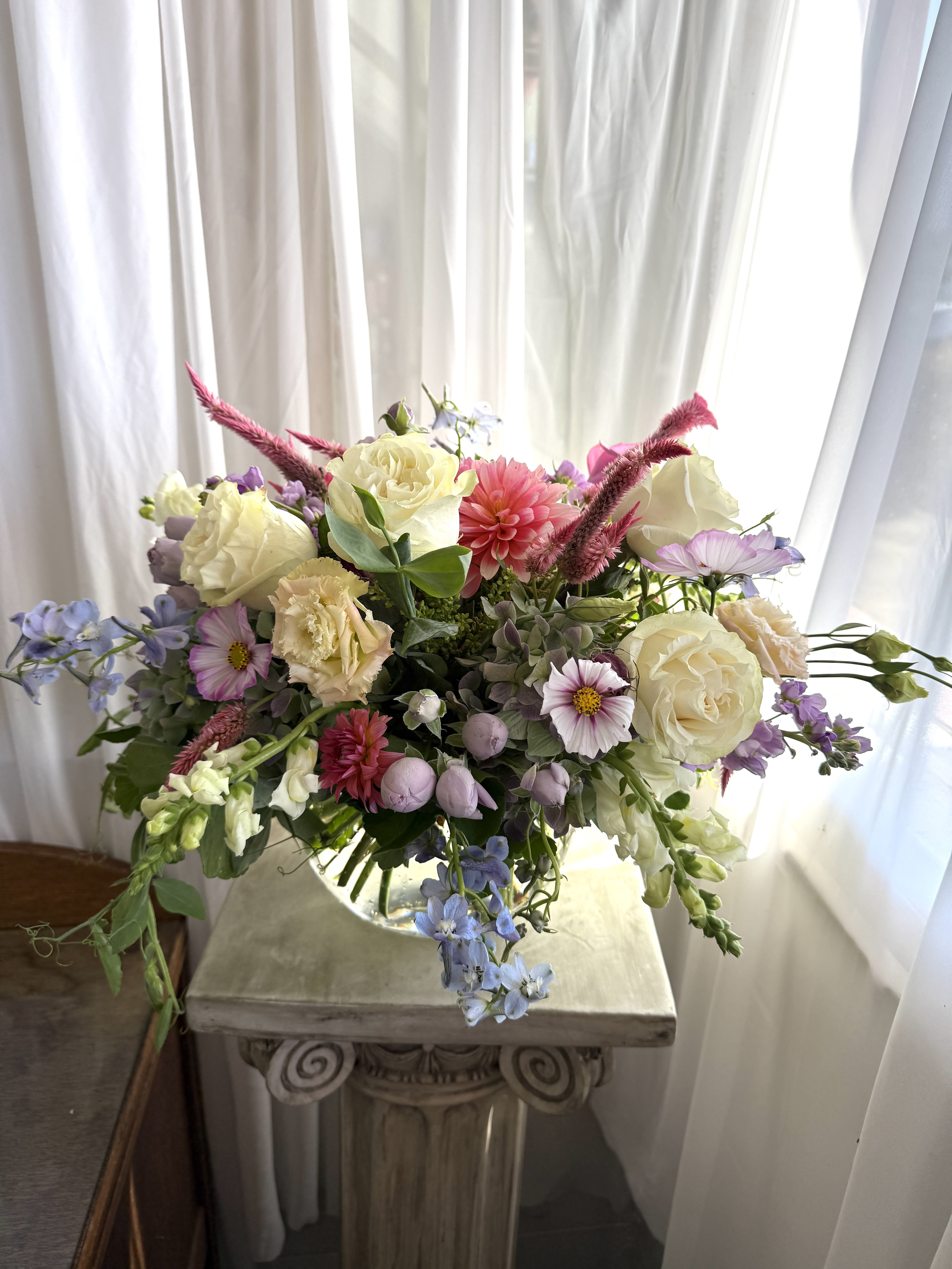 Mixed bouquet of cream, pink, and lavender flowers in a glass vase