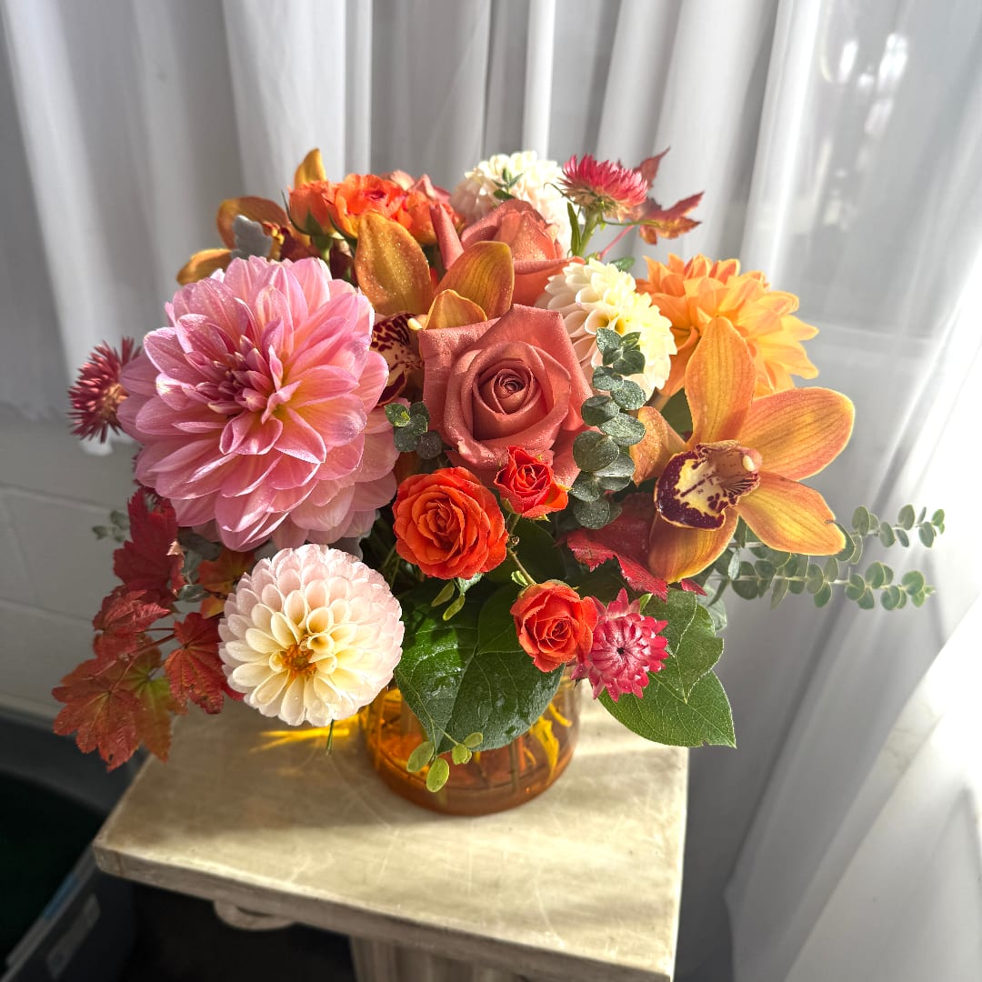Colorful bouquet of dahlias, roses, and orchids in an amber glass vase