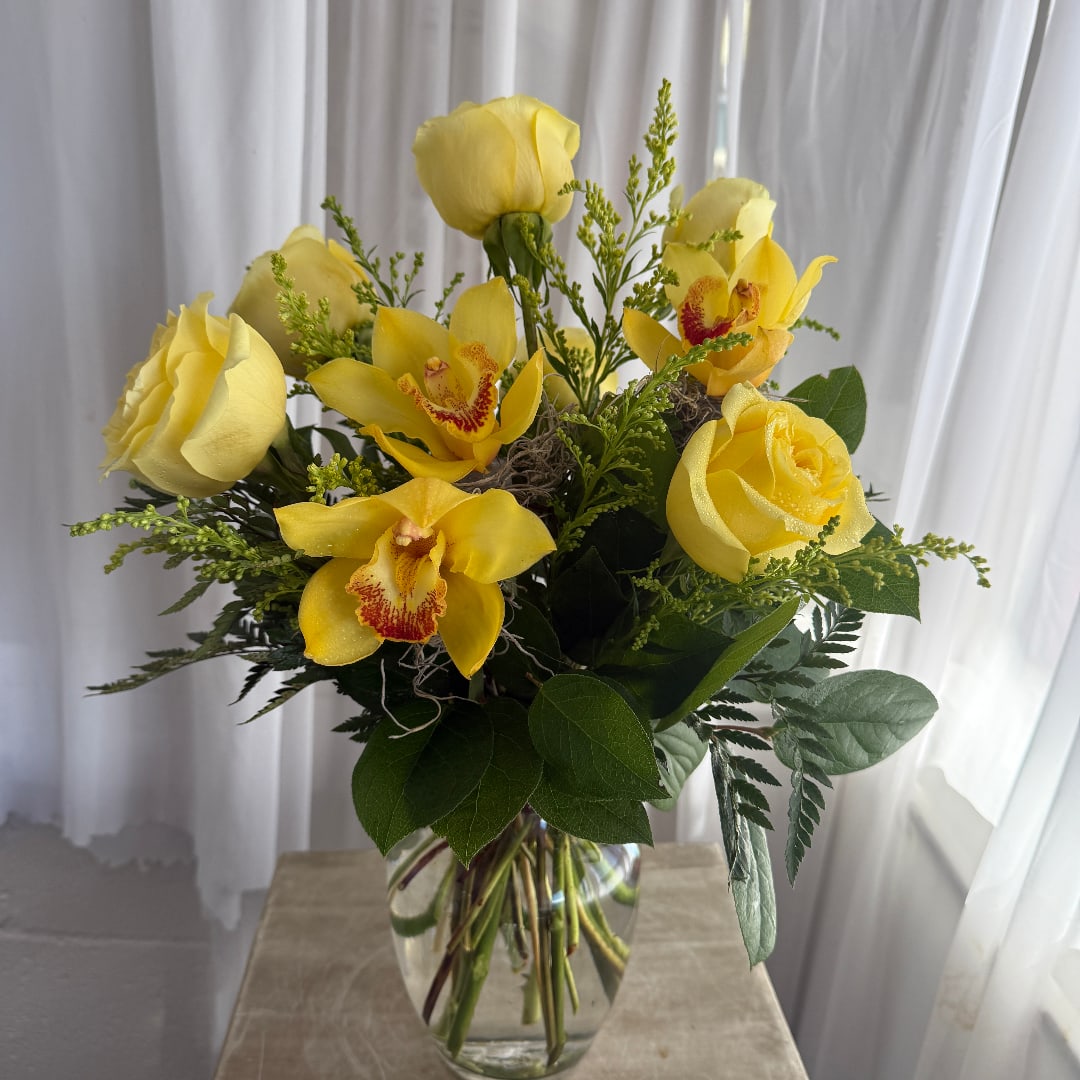 Yellow roses and orchids arranged in a clear glass vase