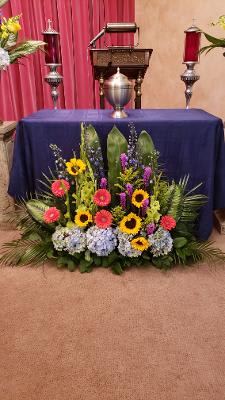 Colorful floral altar arrangement with sunflowers, gerbera daisies, and hydrangeas