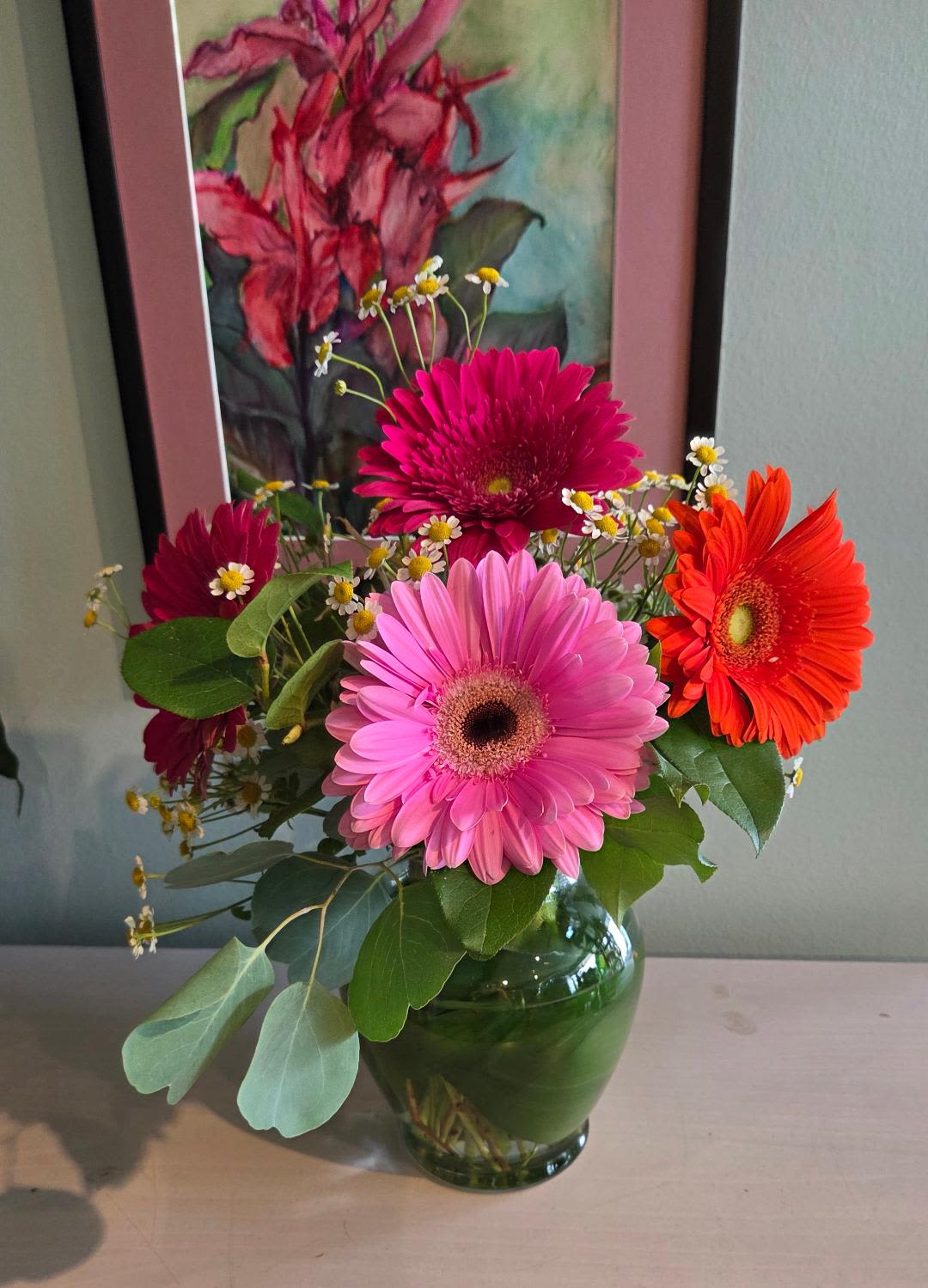 Bright pink and orange gerbera daisies with small white daisies in a clear glass vase.