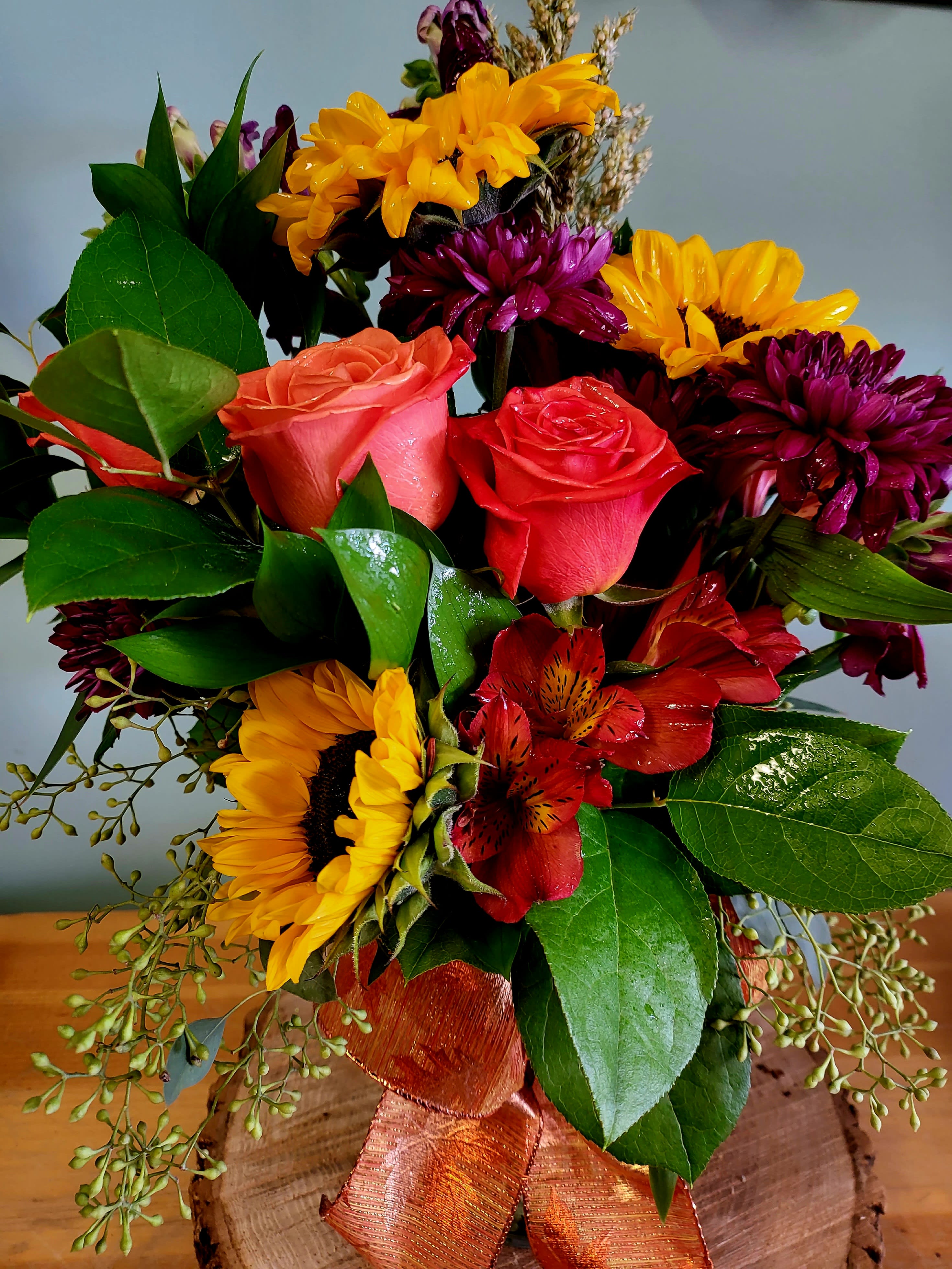 Bouquet of sunflowers, roses, and red alstroemeria with an orange ribbon