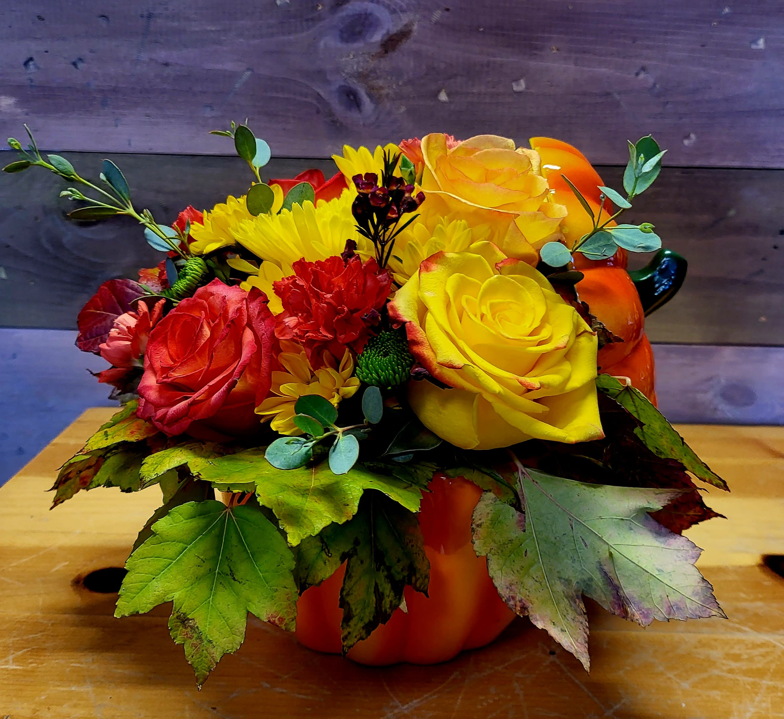 Bouquet of yellow and red roses with daisies in a pumpkin container