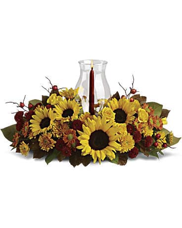 Sunflower Centerpiece - Symbolizing warmth and happiness, it is no wonder the sunflower is a quintessential ingredient in so many fall bouquets. This centerpiece maximizes the joy of sunflowers by arranging them with a bevy of fall flowers, foliage and a cranberry hued candle under hurricane glass.  Along with brilliant sunflowers, you'll find yellow spray roses, bronze and rust chrysanthemums, red berries, magnolia leaves and of course an elegant tapered candle inside a hurricane vase.