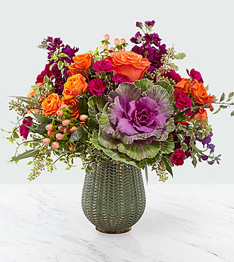 Autumn Harvest Bouquet - The Autumn Harvest Bouquet is both simple and simply unforgettable. This collection of flowers takes all the vibrant colors fall and brings them together in a unique way in a muted green ceramic vase with a gold metallic finish. Ornamental kale is surrounded by orange roses, spray roses and purple stock making the perfect gift for you or your loved ones.  14H x 15W