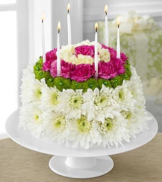 Tiered floral cake with white daisies, pink carnations, and candles