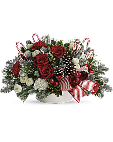Christmas arrangement with red roses, white blooms, candy canes, and pinecones in a white bowl