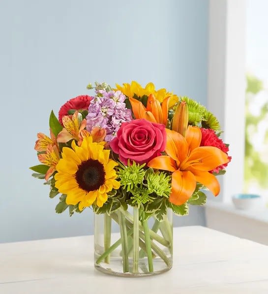 Floral Embrace - Product ID: 100299  Send our truly original arrangement to let your special someone embrace their inner interior decorator. Crafted by our expert florists from the freshest roses, lilies, stock, sunflowers and alstroemeria in a classic cylinder vase, its compact beauty is perfect for impressing friends and family or for simply dressing up any room in the home. Vibrant arrangement of roses, lilies, sunflowers, stock, alstroemeria, poms and monte casino, gathered with fresh salal Artistically designed in an elegant glass cylinder vase; measures 6"H Large arrangement measures approximately 13"H x 13"L Medium arrangement measures approximately 12"H x 12"L Small arrangement measures approximately 11"H x 11"L Our florists hand-design each arrangement, so colors, varieties, and basket may vary due to local availability Lilies may arrive in bud form and will open to full beauty over the next 2-3 days