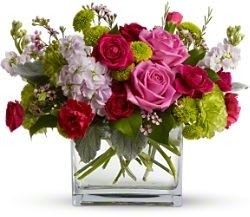 Pink and red roses in a clear square vase with green accents