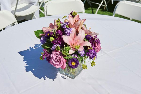 Pink and purple floral centerpiece in a square glass vase