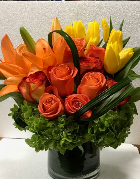 Orange roses and yellow tulips arranged in a glass vase