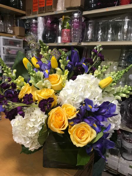 Bouquet of yellow roses, white hydrangeas, and purple flowers in a vase