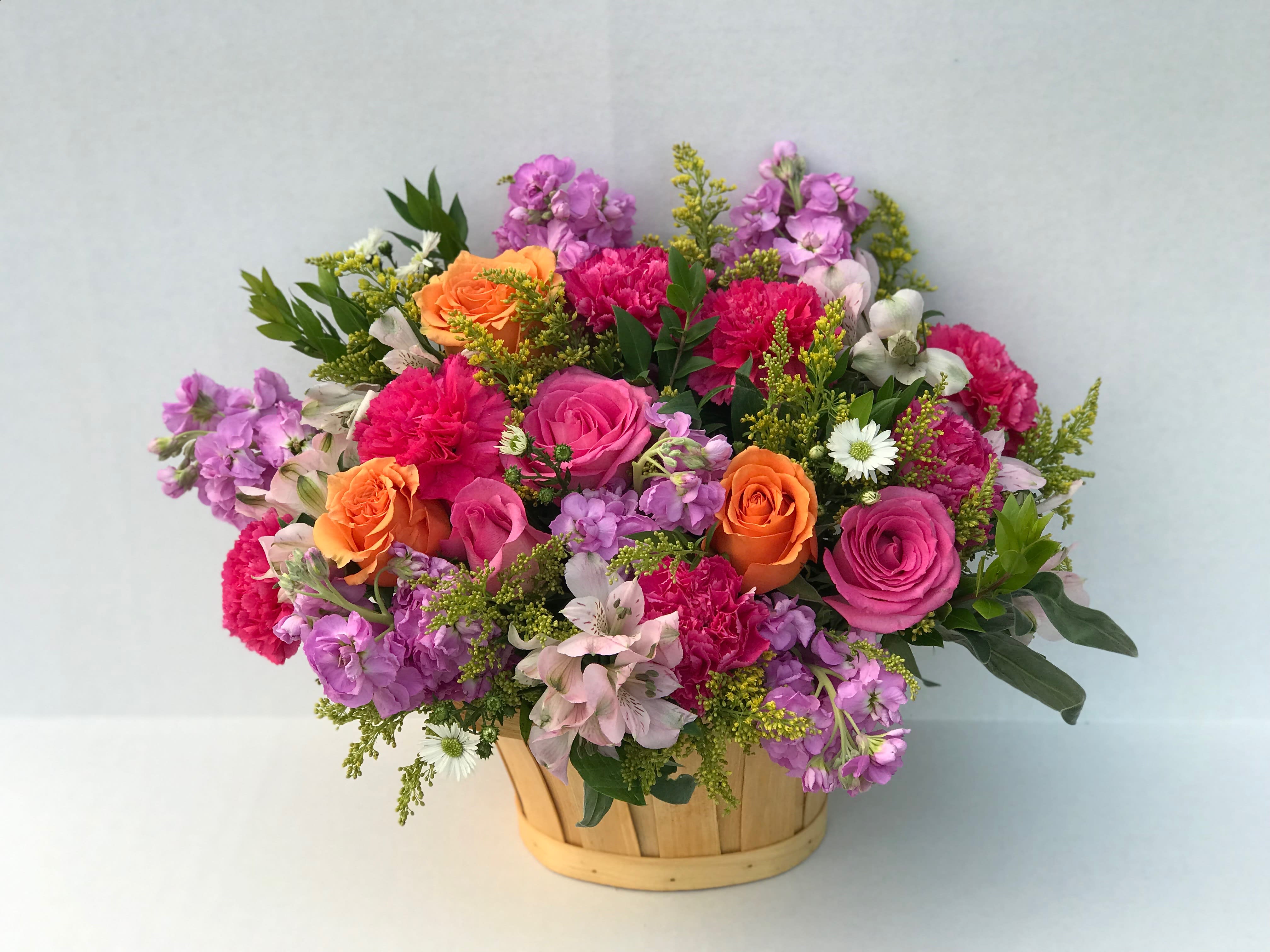 Mixed bouquet of pink, purple, and orange flowers in a wooden basket