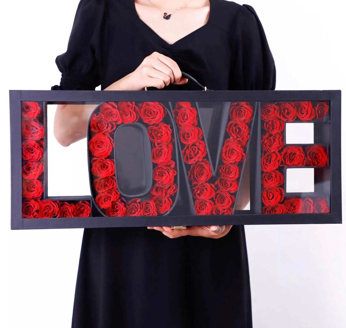 Framed LOVE sign filled with red roses, held by a person in black
