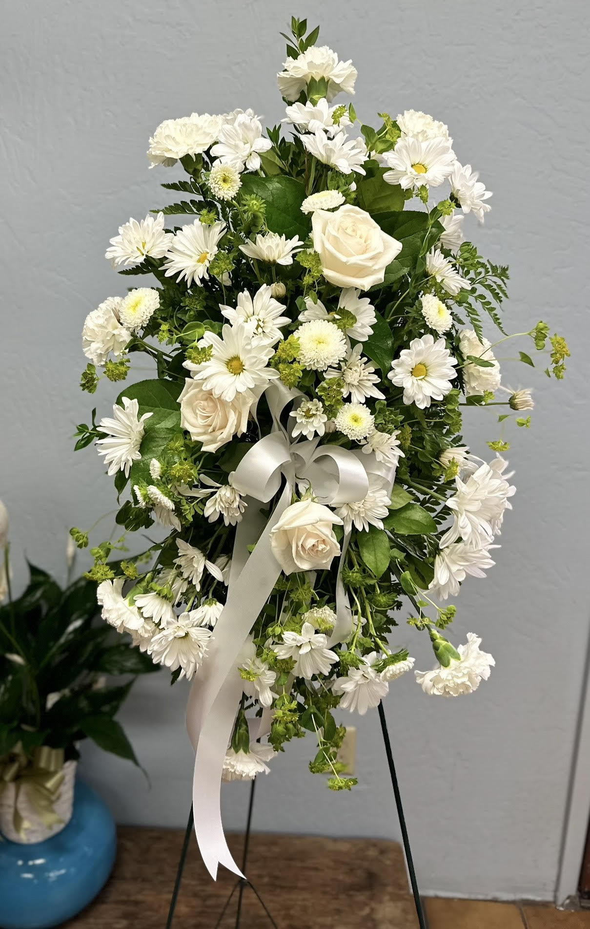 White floral standing spray with roses, daisies, and ribbon