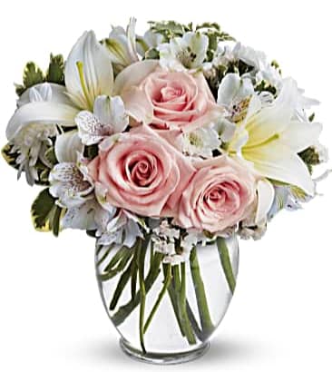 Round glass vase arrangement with pale pink roses, white lilies, and white accent flowers.