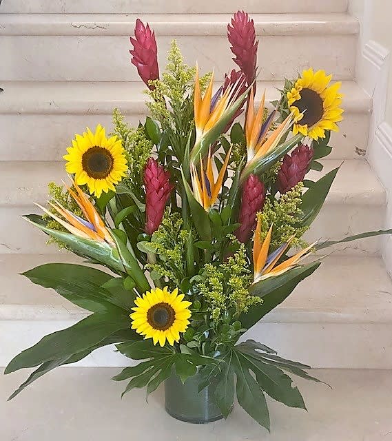 Tall tropical arrangement with yellow sunflowers and orange bird-of-paradise in a glass vase
