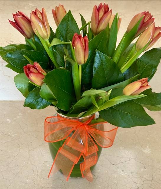 Bouquet of orange and peach tulips in a clear vase with an orange ribbon bow