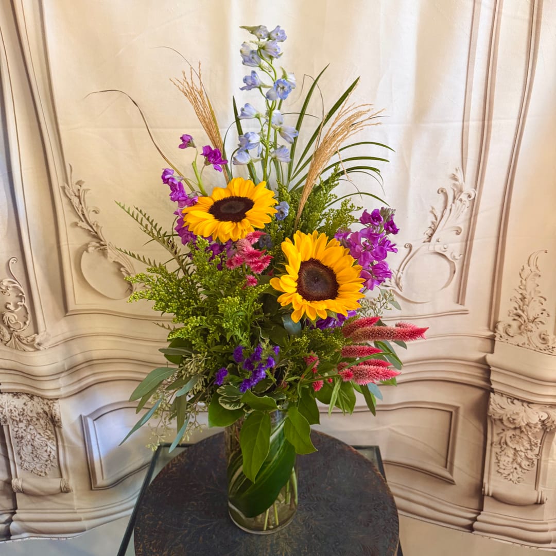 Tall mixed bouquet with sunflowers, purple blooms, and a glass vase