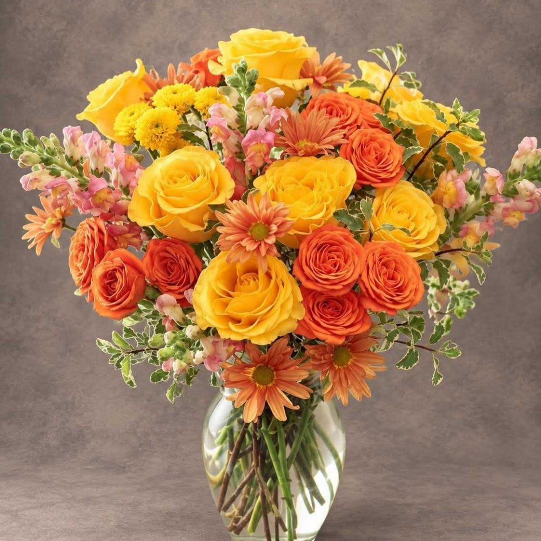 Yellow and orange roses with daisies in a clear glass vase