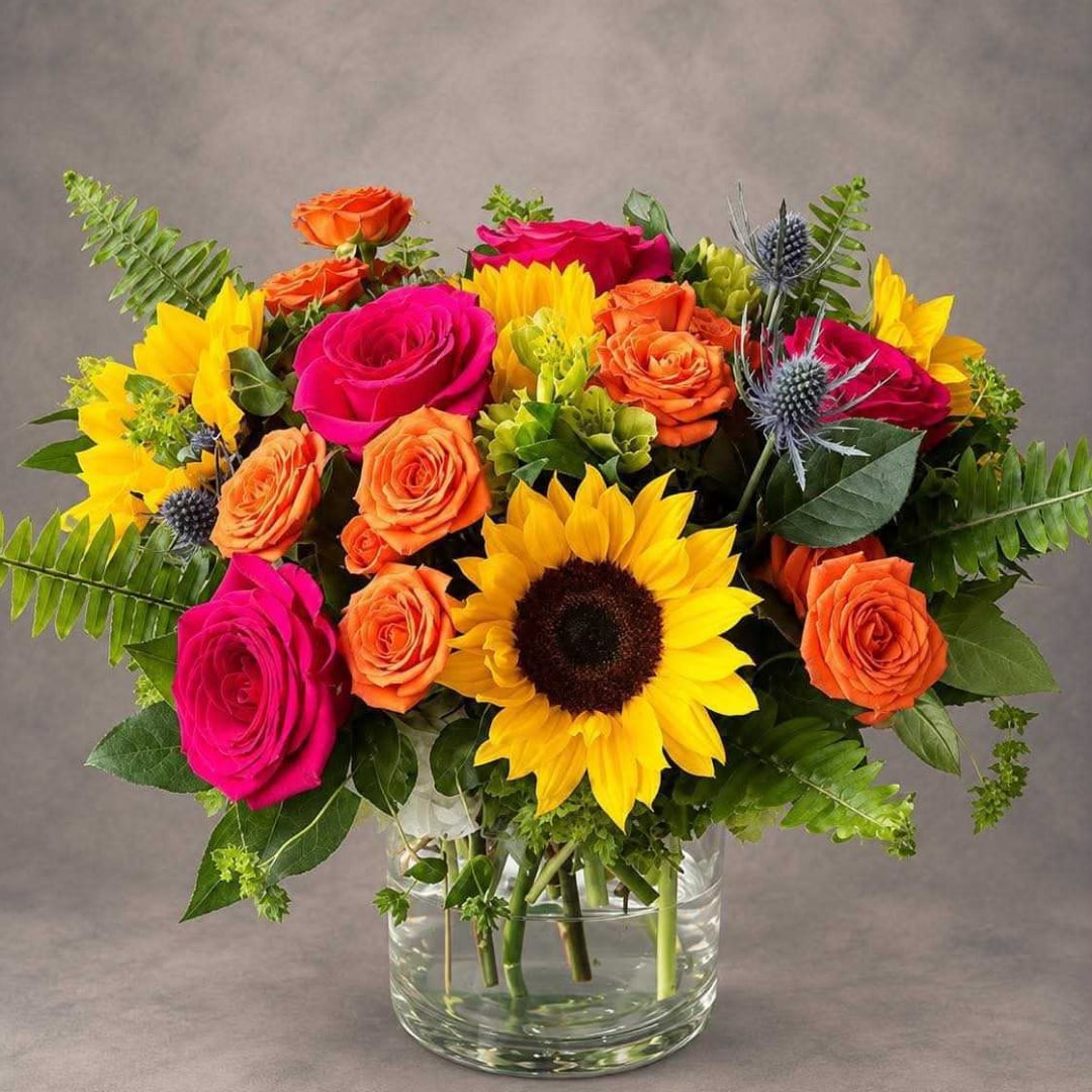 Bright mixed bouquet with roses and a sunflower in a glass vase