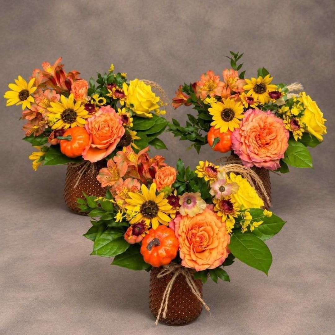 Three autumn floral arrangements with orange roses and yellow daisies in brown vases