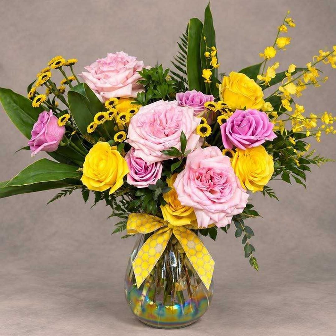 Pink and yellow roses in a glass vase with a yellow ribbon