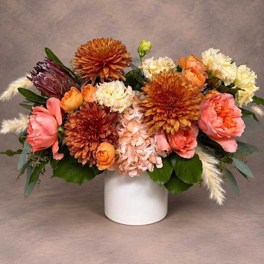 Mixed bouquet of orange, pink, and cream flowers in a white vase