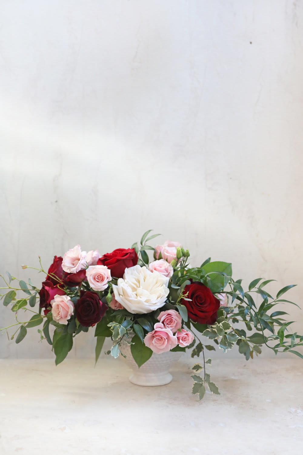 Low arrangement of red, pink, and white roses in a white vase