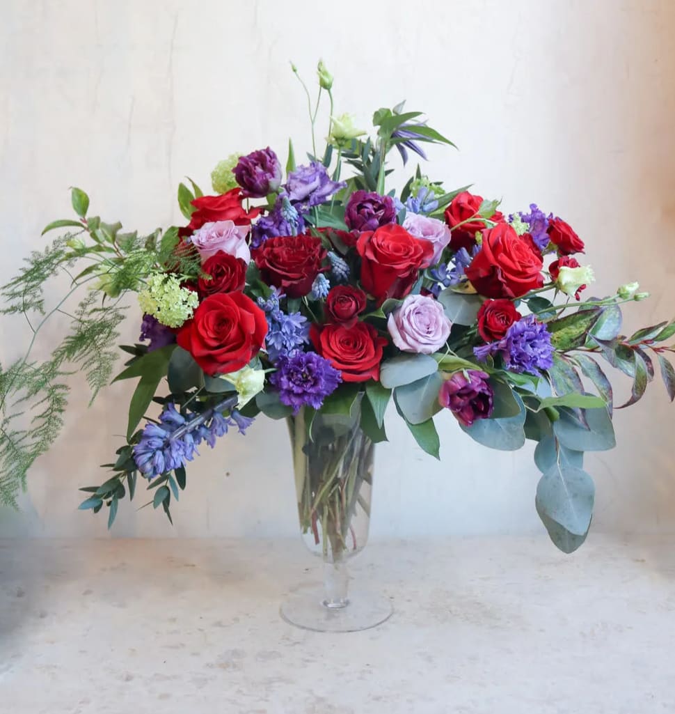 Mixed bouquet of red, purple, and pink roses in a clear glass vase