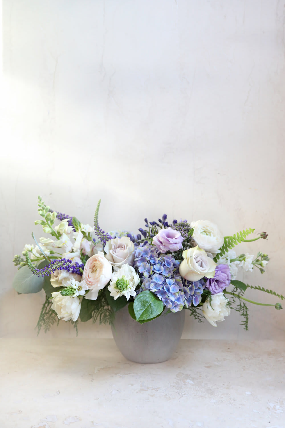 Low floral arrangement in a gray vase with white, lavender, and blue blooms