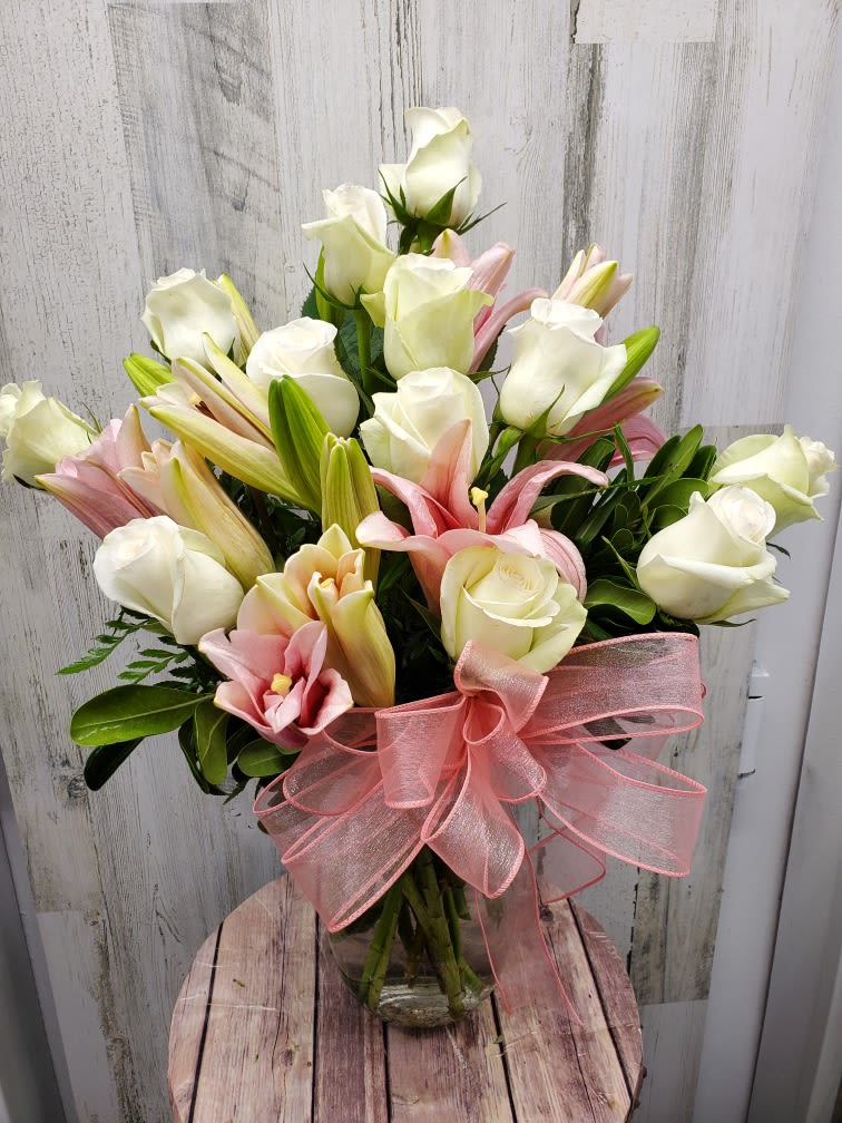Bouquet of white roses and pink lilies in a glass vase with a pink ribbon