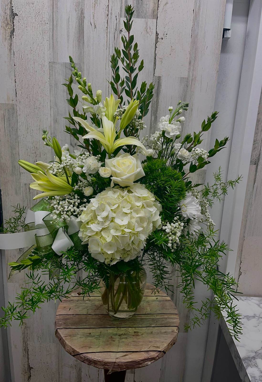 White floral arrangement with lilies, roses, and hydrangea in a glass vase