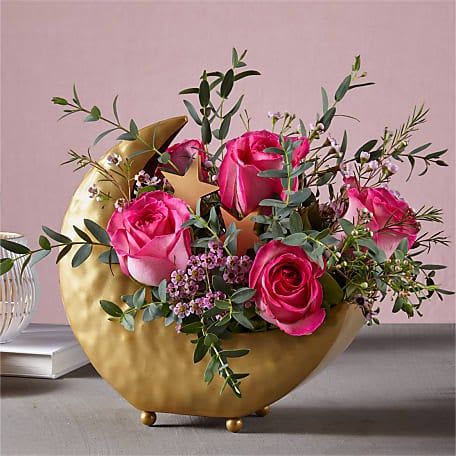 Pink roses arranged in a gold crescent vase with greenery