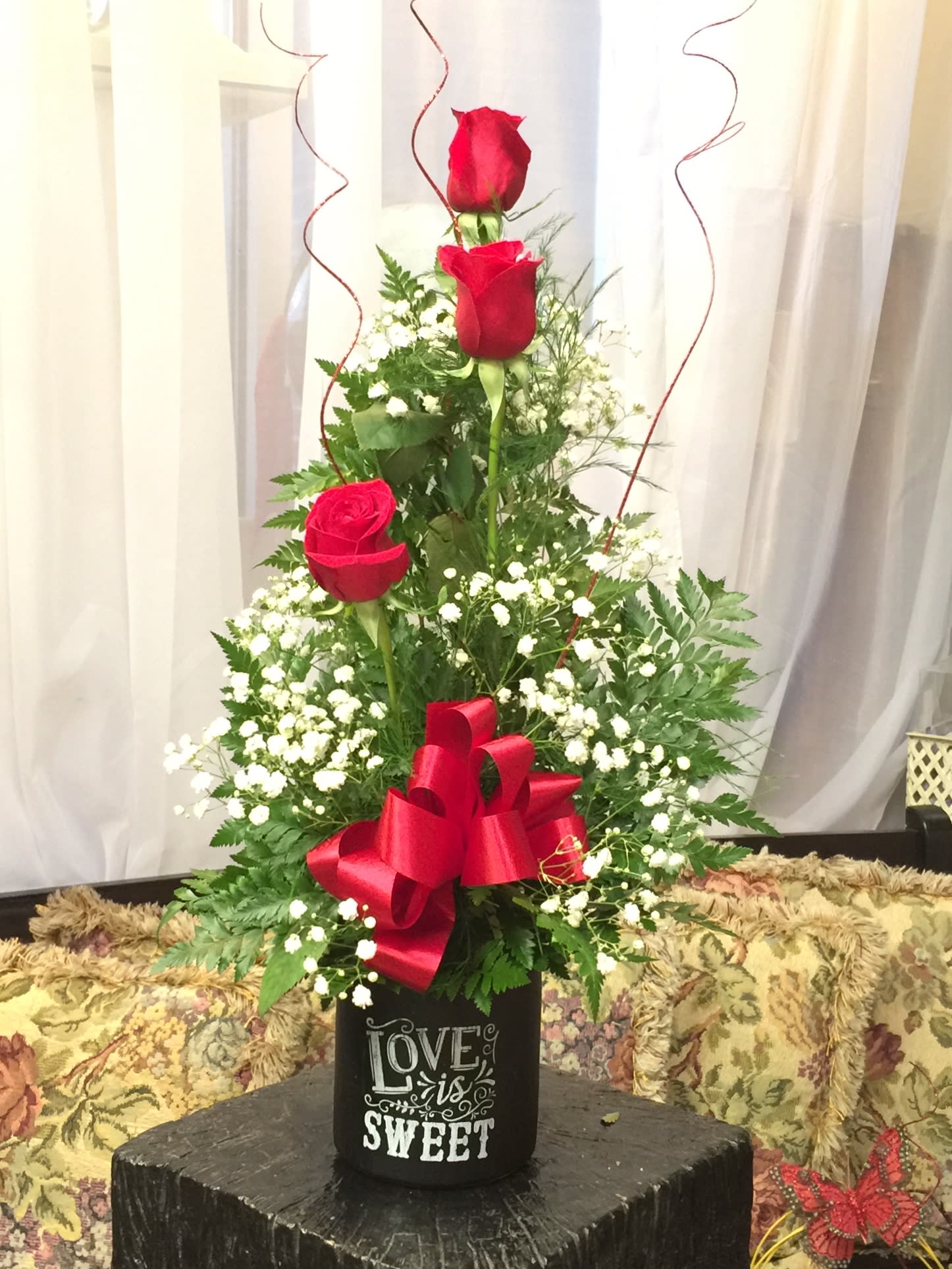 Tall arrangement of red roses with baby's breath in a black container