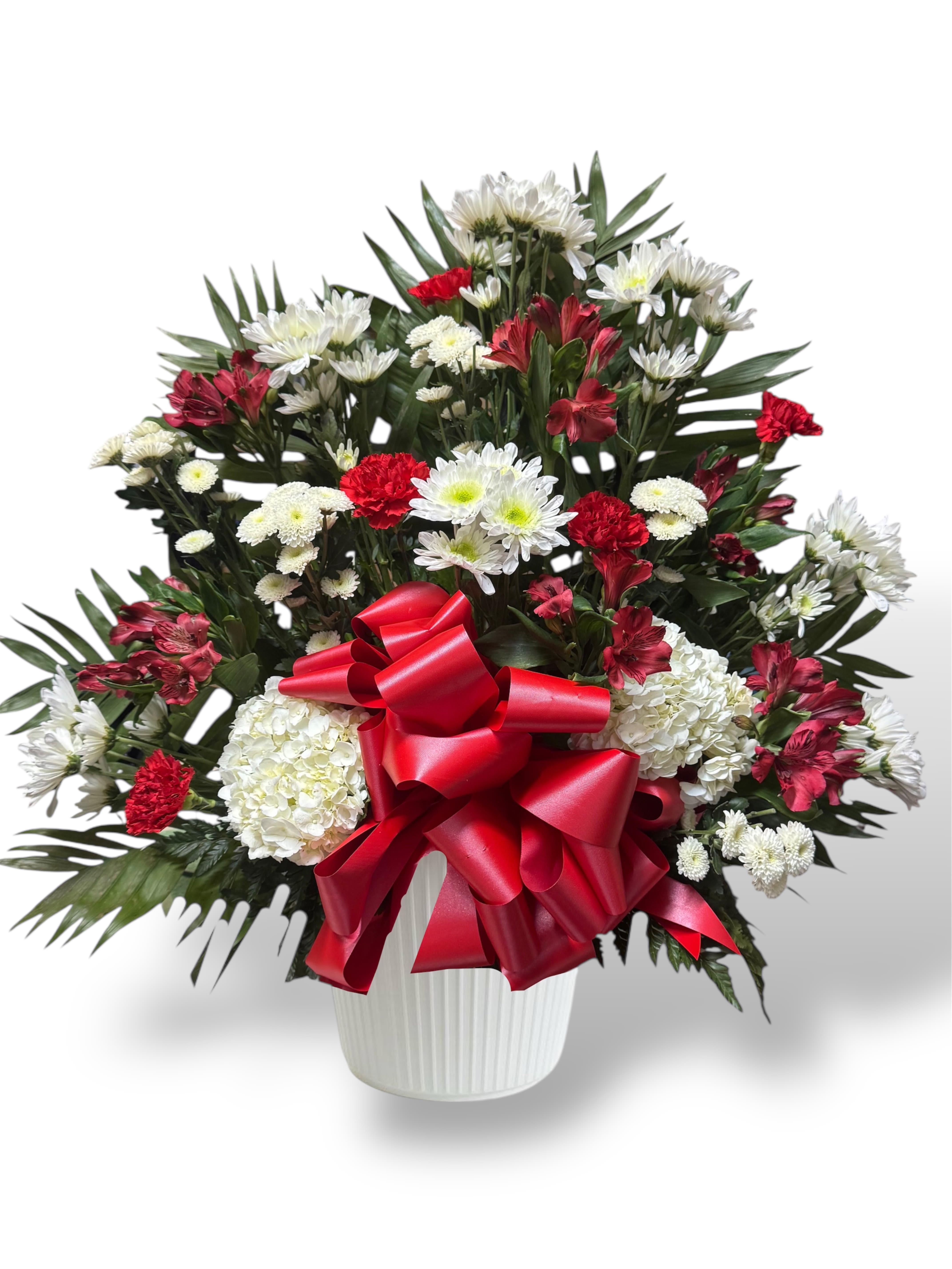 Red and white mixed flower arrangement in a white vase with a red bow