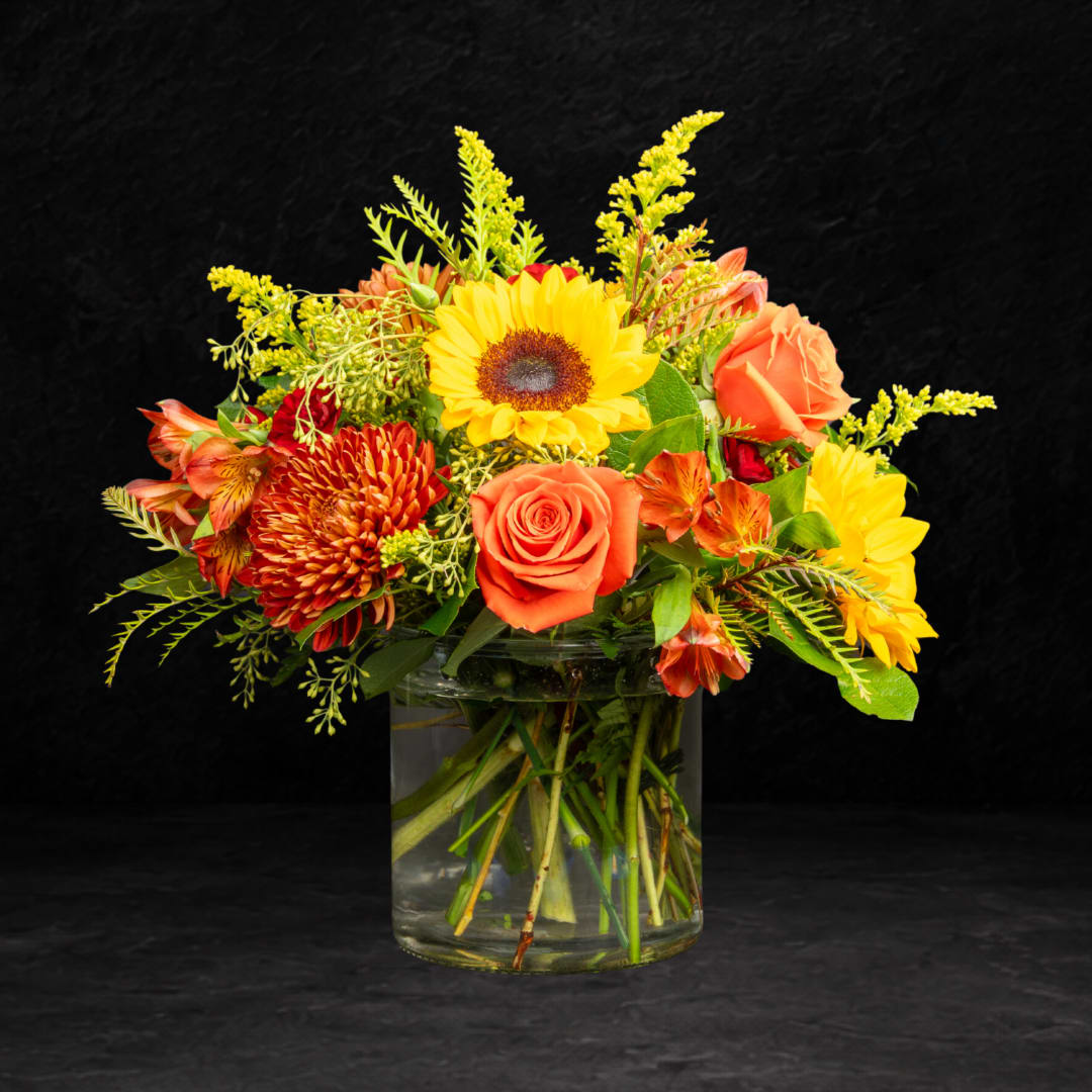 Mixed bouquet of sunflowers, roses, and orange blooms in a glass vase