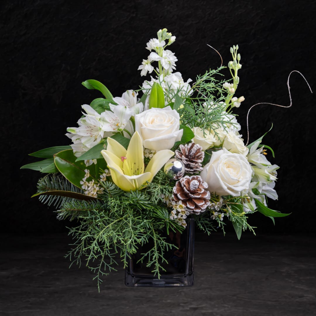 White roses and lilies in a black vase with pinecones