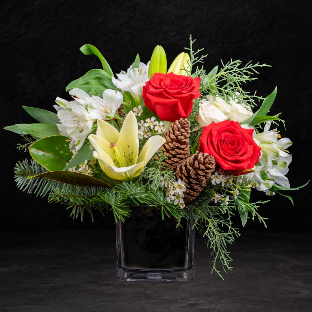 Red roses and white lilies in a black glass vase with pinecones