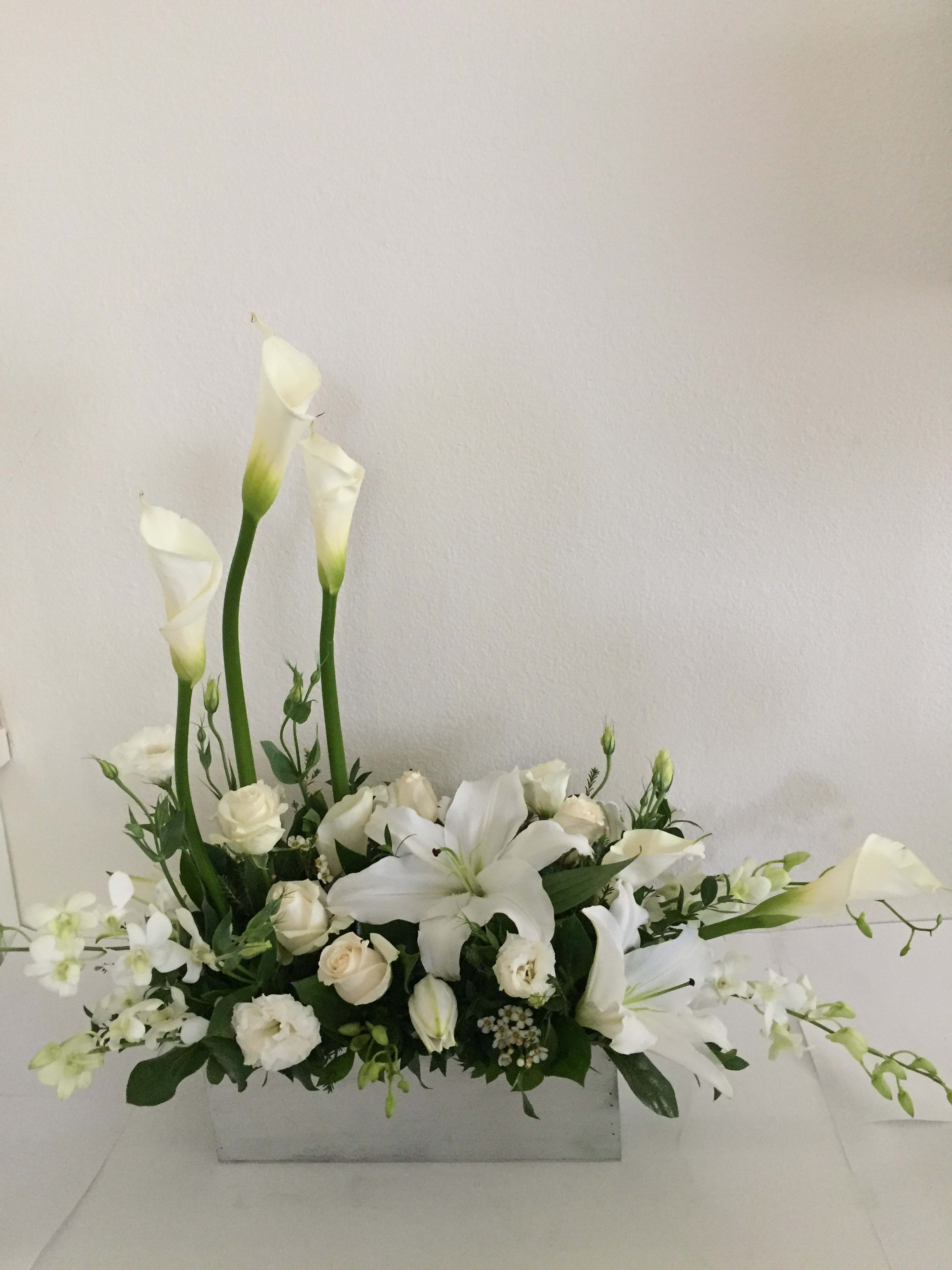 White floral arrangement with calla lilies, roses, and a lily in a rectangular vase
