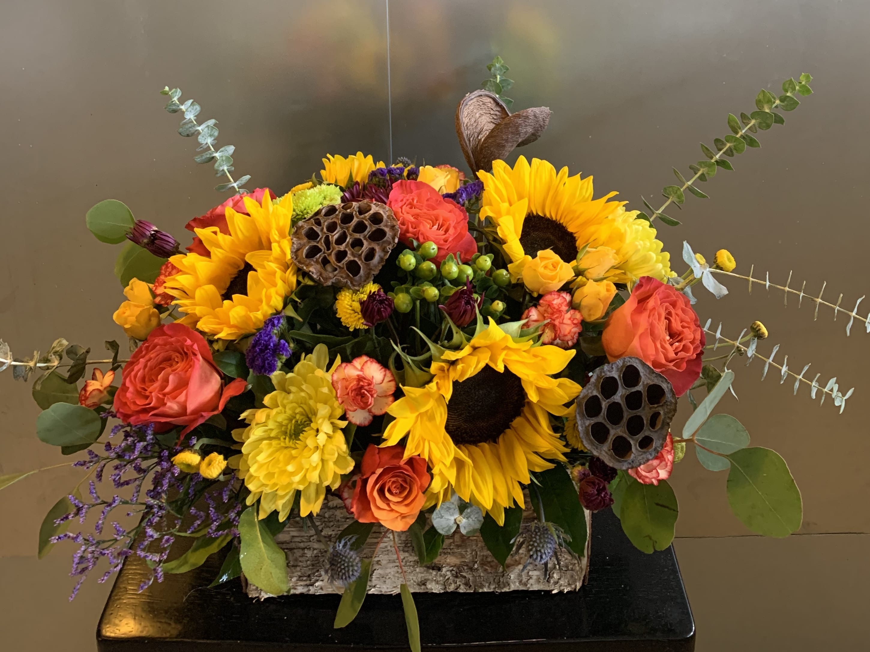 Bright mixed bouquet with sunflowers, roses, and lotus pods in a rustic container