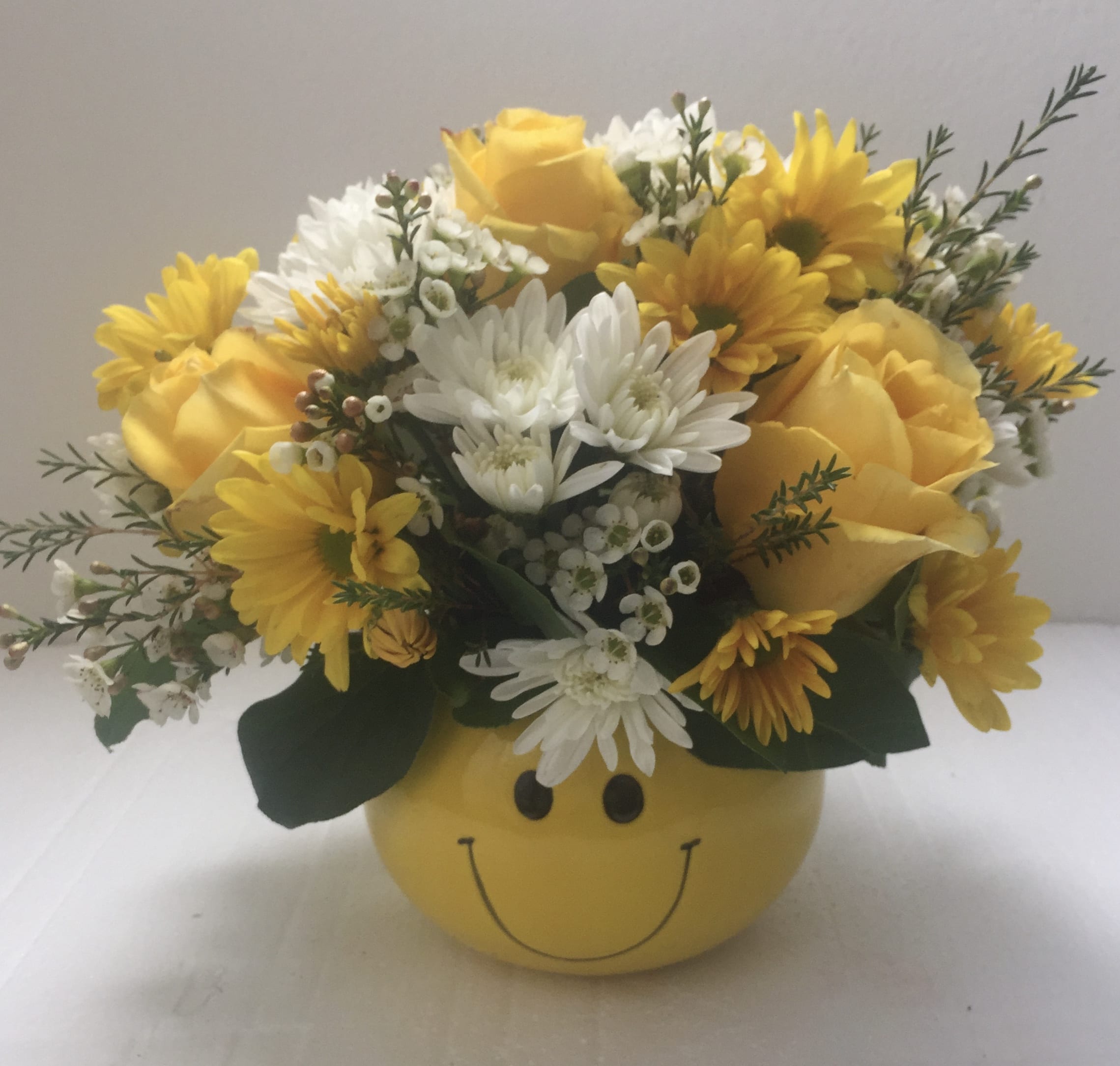 Yellow and white flower arrangement in a smiley-face container