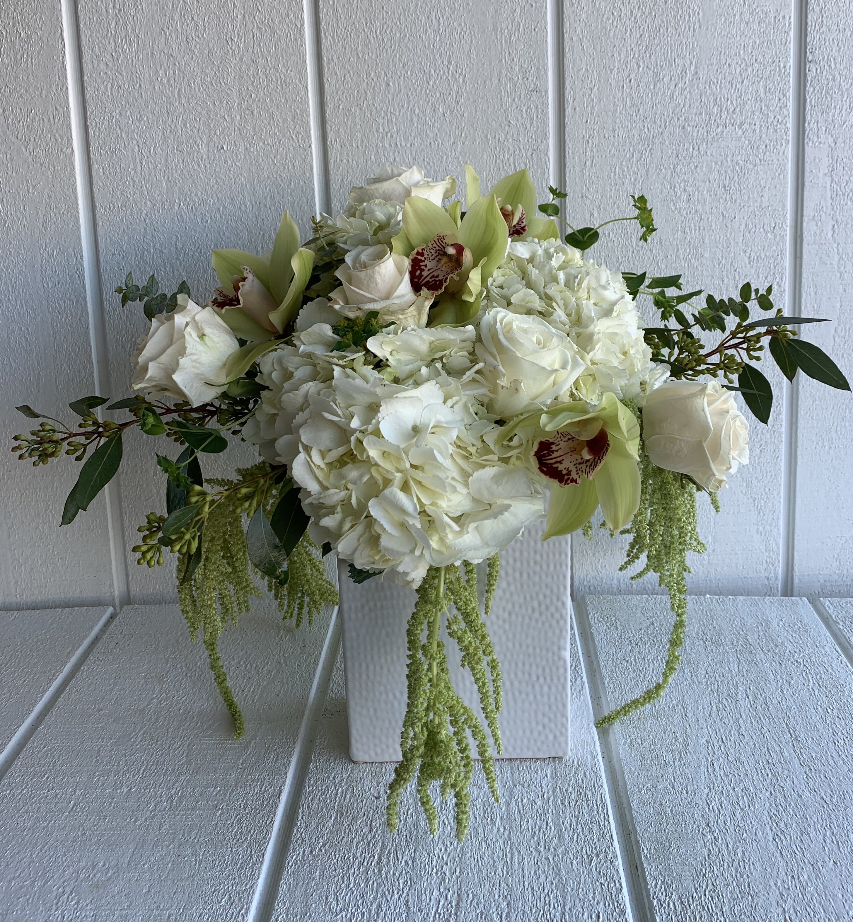 White floral arrangement with roses, hydrangeas, and green orchids in a white vase