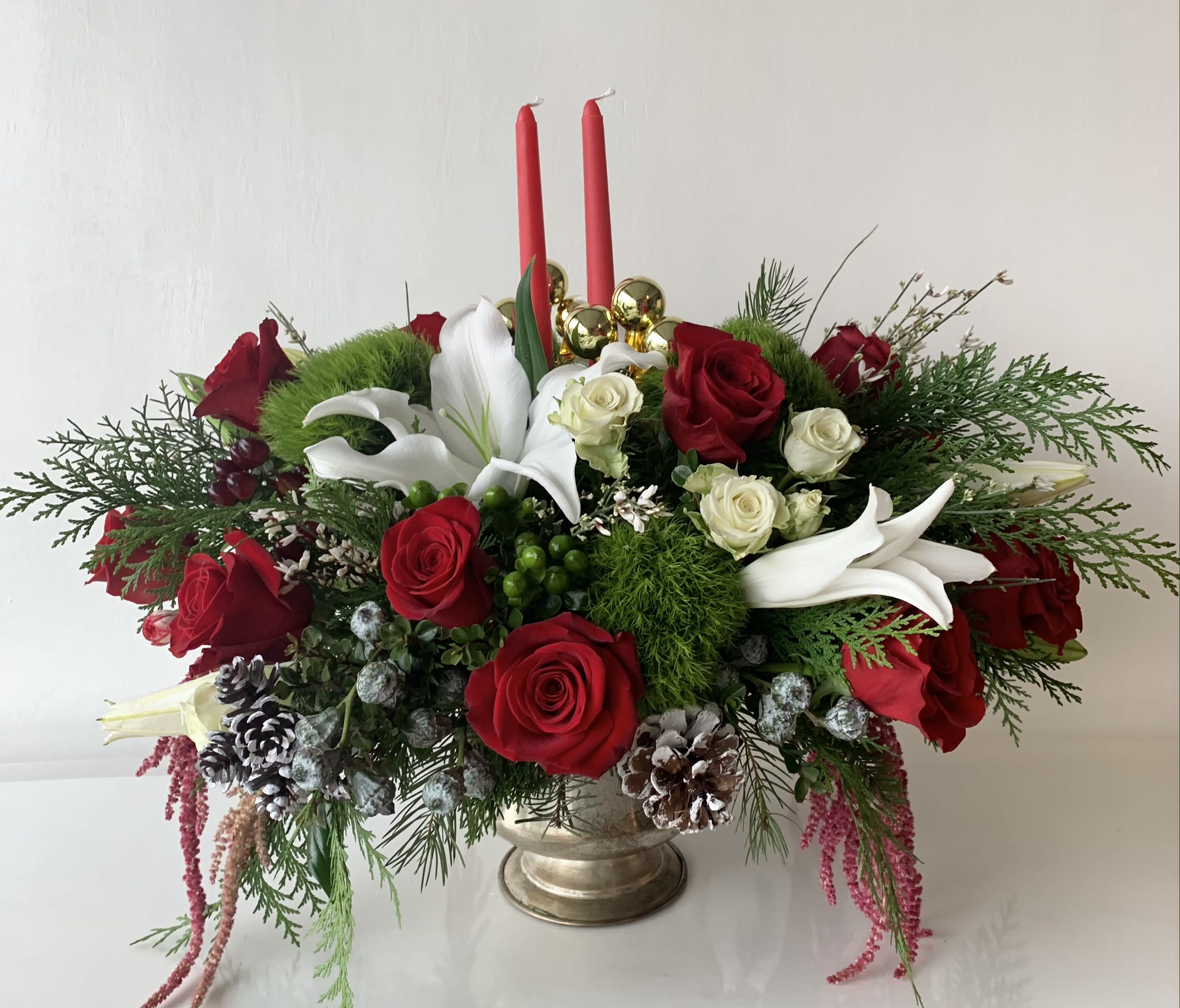 Red roses and white lilies arranged in a gold vase with two red candles