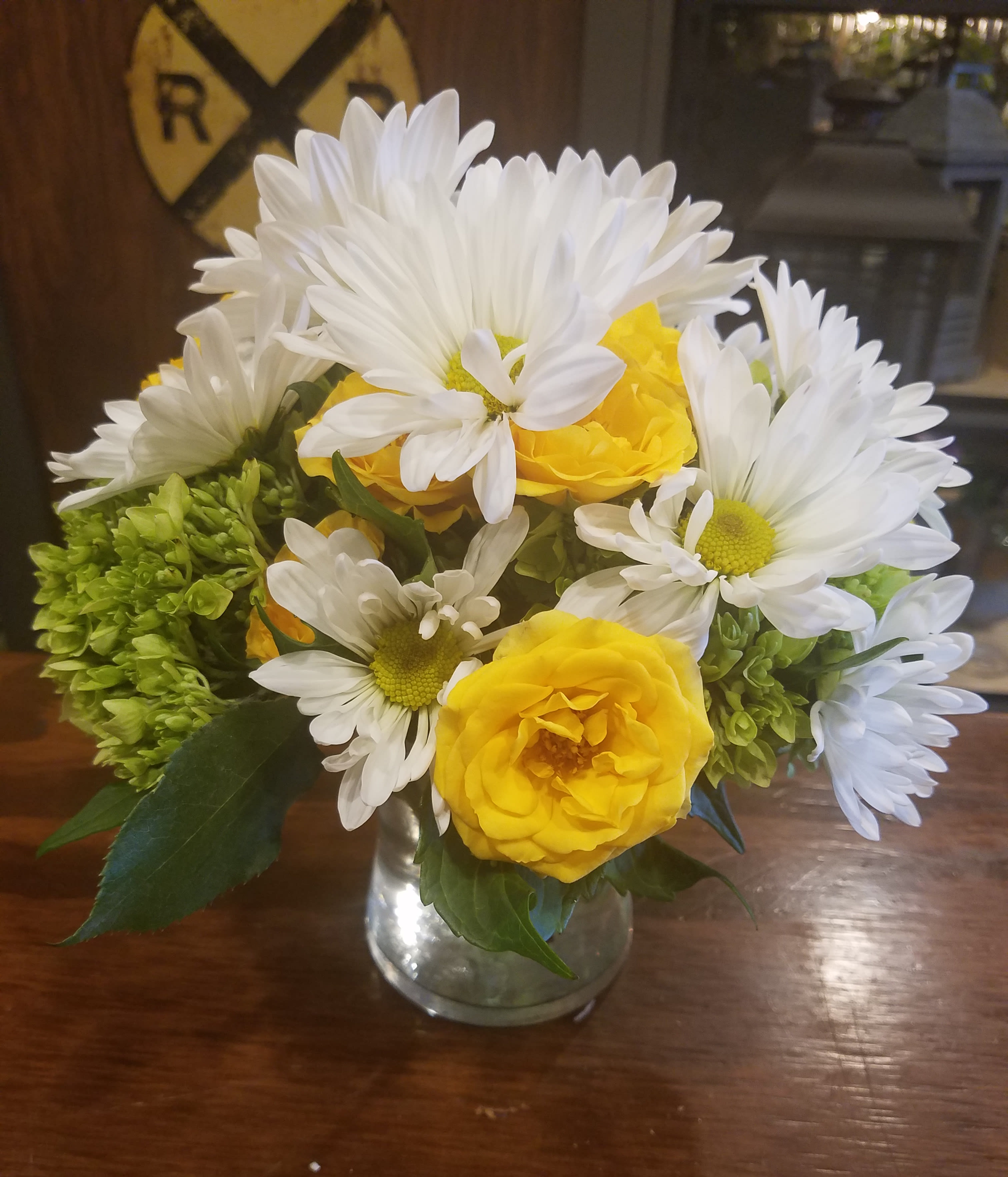 Yellow roses and white daisies arranged in a clear glass vase